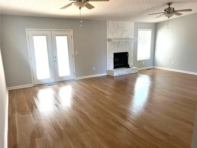 an empty room with wooden floor fireplace and windows