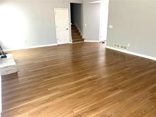 a view of an empty room with wooden floor and stairs
