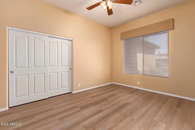 an empty room with wooden floor chandelier fan and windows