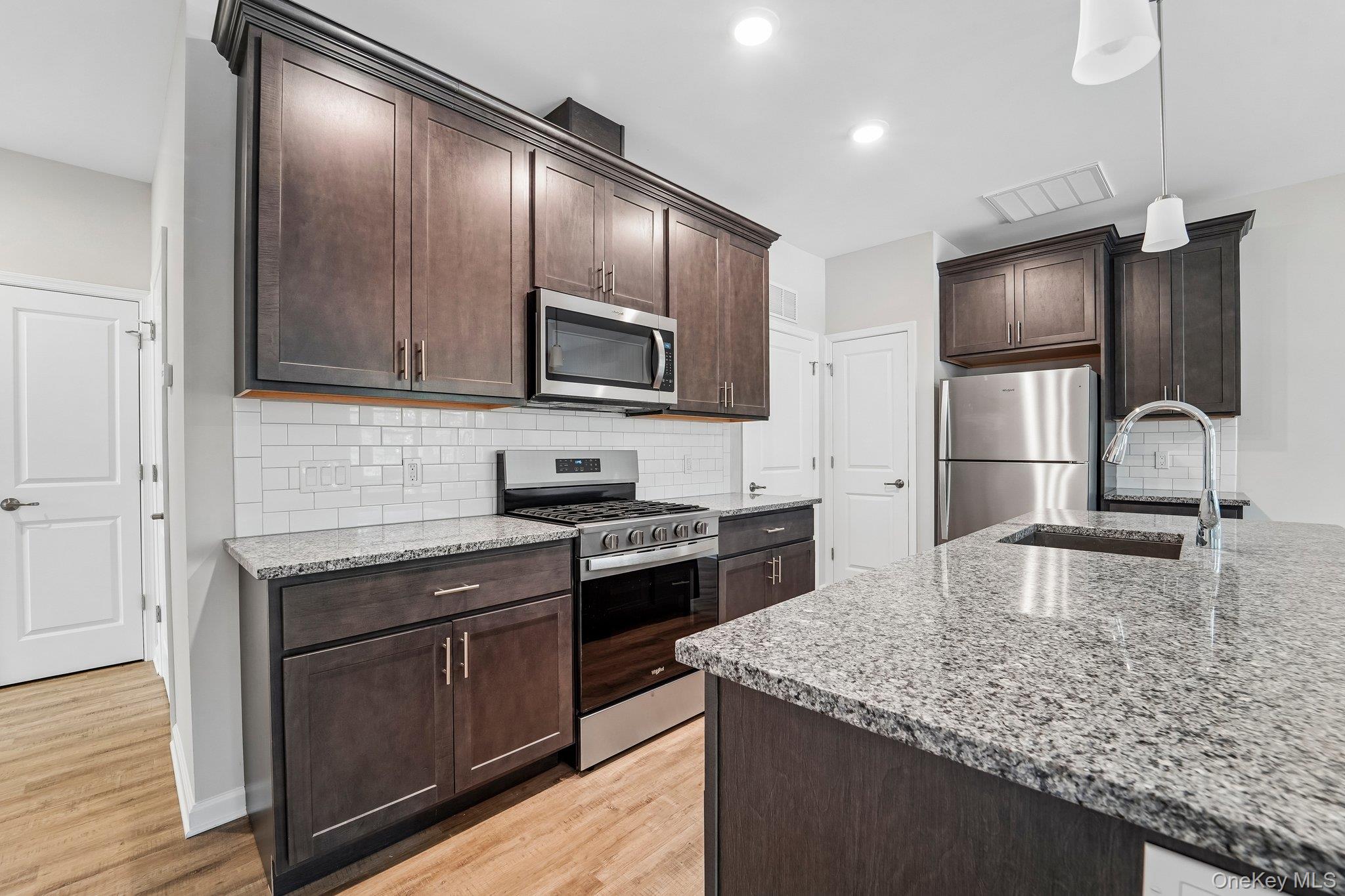 420 Tower Ridge Circle Middletown, NY 10941 - Photo 3 of 25 Modern kitchen featuring rich wood cabinetry, granite countertops, stainless steel appliances, a gas range, subway-tile backsplash, and a large center island with sink and seating.