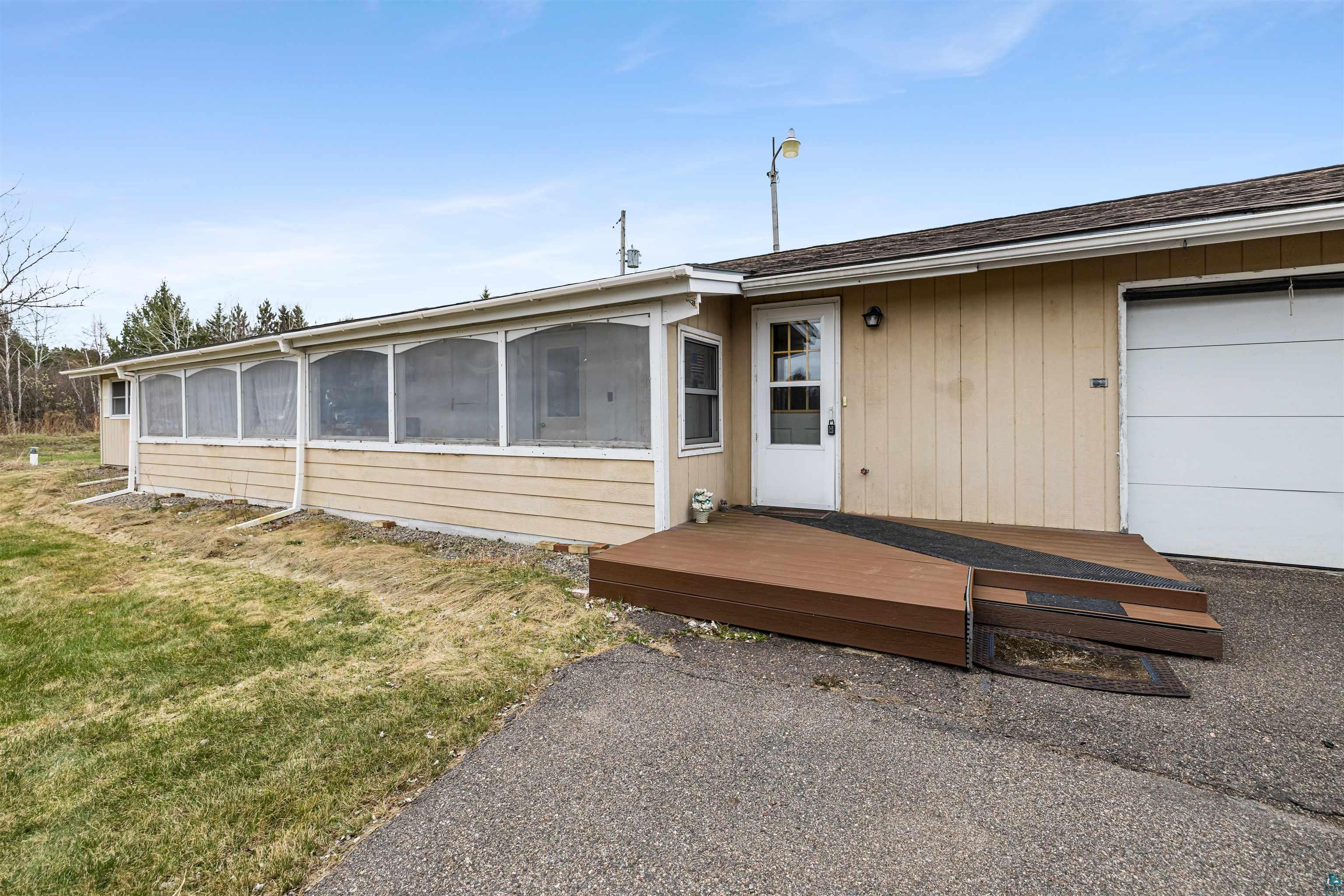 11574 Town Line Road Hibbing, MN 55746 - Photo 24 of 41 Exterior featuring a screened-in porch, tan siding, an attached garage, a white entry door, and a brown composite deck with a ramp