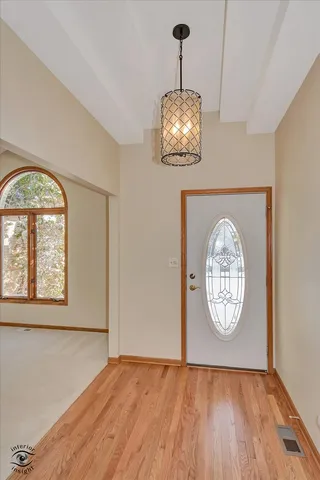 an empty room with wooden floor a chandelier and a window
