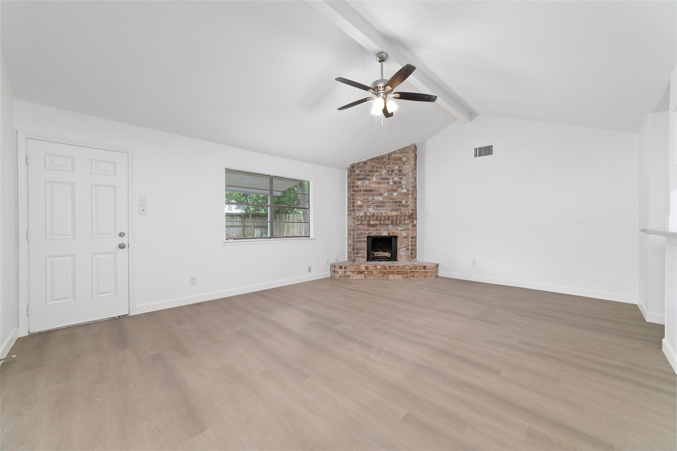 5023 Monteith Drive Spring, TX 77373 - Photo 5 of 20 Spacious living area with vaulted ceilings and a ceiling fan, featuring a cozy fireplace and large window that brings in natural light and creates a warm, inviting atmosphere.