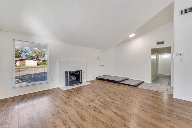 an empty room with wooden floor fireplace and windows