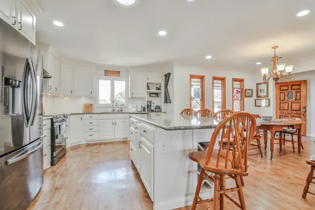 a kitchen with stainless steel appliances granite countertop a stove refrigerator a dining table and chairs with wooden floor