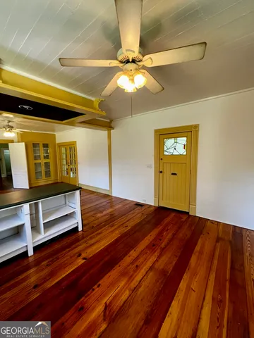 a view of an empty room with wooden floor and fan