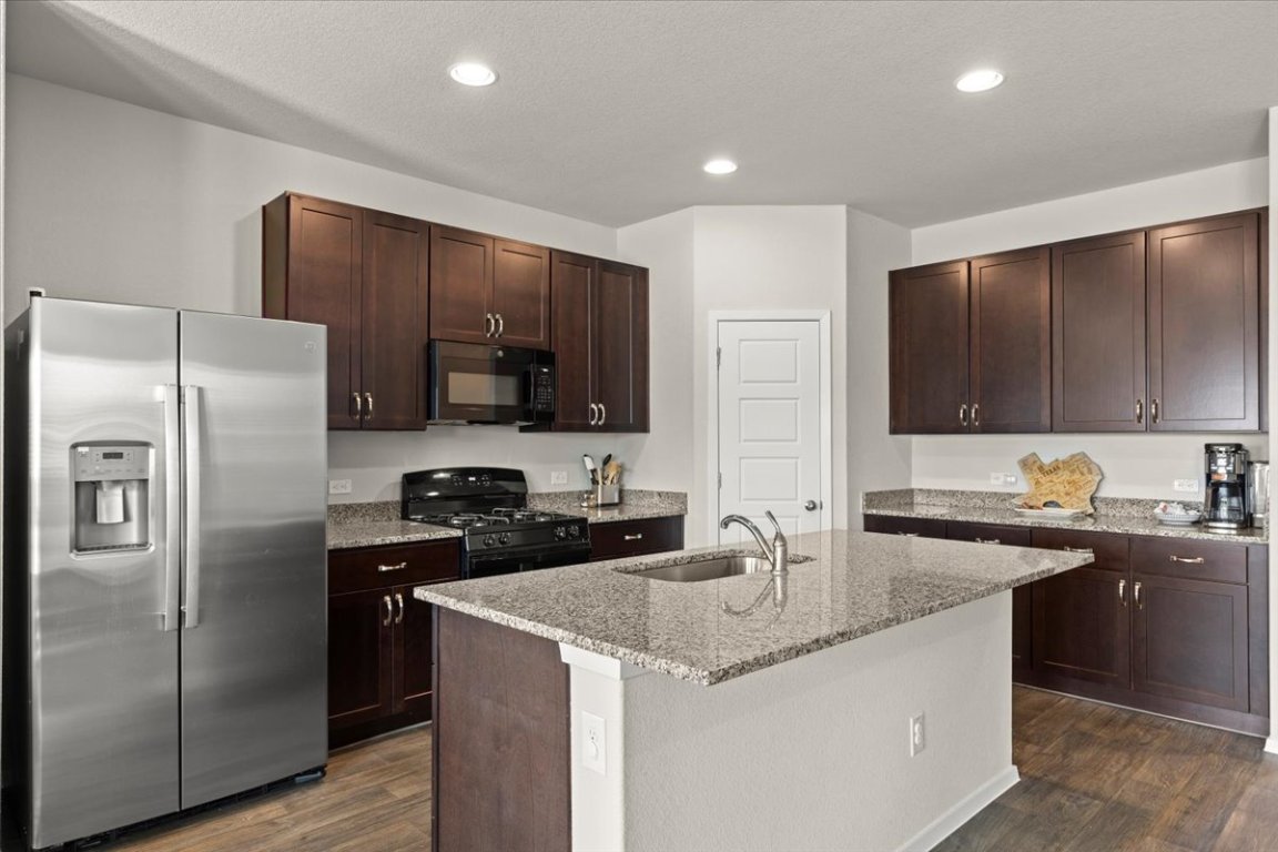 1296 Teychas Drive Kyle, TX 78640 - Photo 12 of 39 Kitchen featuring black appliances, a sink, dark wood finished floors, dark brown cabinets, and light stone counters