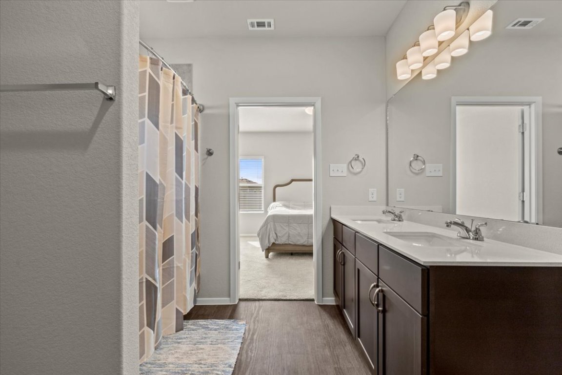 1296 Teychas Drive Kyle, TX 78640 - Photo 17 of 39 Bathroom featuring wood finished floors, double vanity, connected bathroom, and baseboards