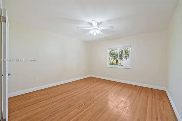 an empty room with wooden floor chandelier fan and windows