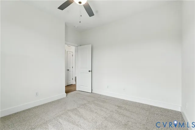 an empty room with chandelier fan and kitchen view