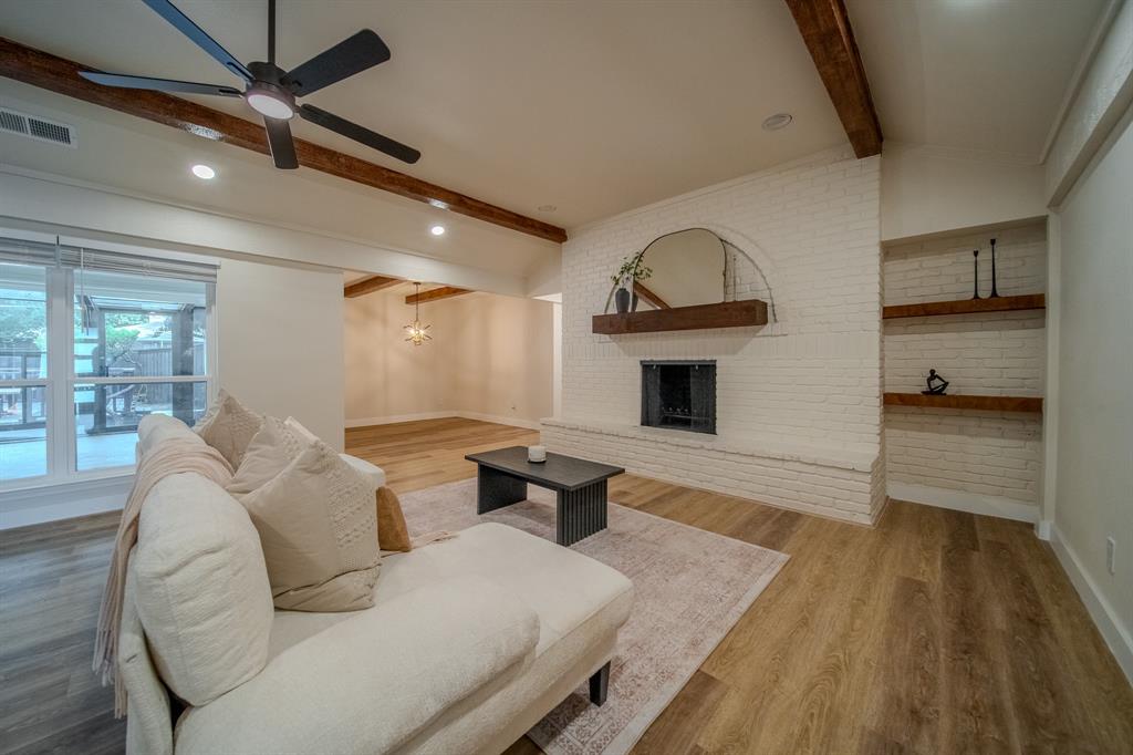5125 Ashbrook Road Dallas, TX 75227 - Photo 12 of 34 Vaulted ceiling with exposed wood beams, wood-finish flooring, white painted brick fireplace with wood mantel, built-in shelving, and recessed lighting
