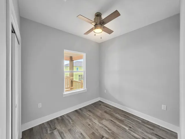 an empty room with wooden floor fan and windows