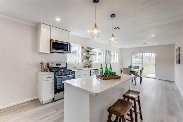 a kitchen with stainless steel appliances kitchen island granite countertop a stove top oven a sink a dining table and chairs with wooden floor