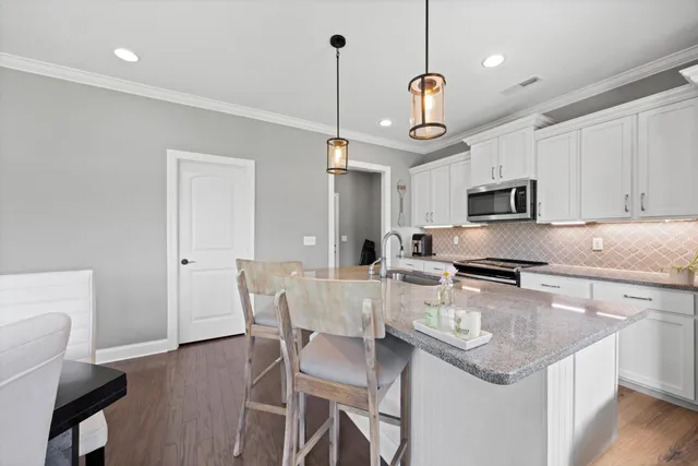 a kitchen with stainless steel appliances granite countertop a sink a stove a dining table and chairs with wooden floor