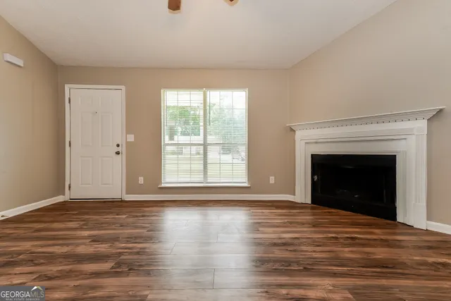a view of an empty room with wooden floor fireplace and a window