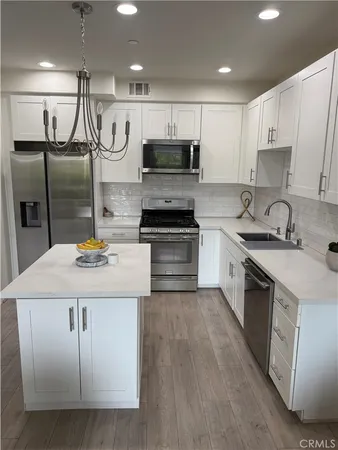 a kitchen with kitchen island granite countertop a sink a stove a refrigerator cabinets and chairs