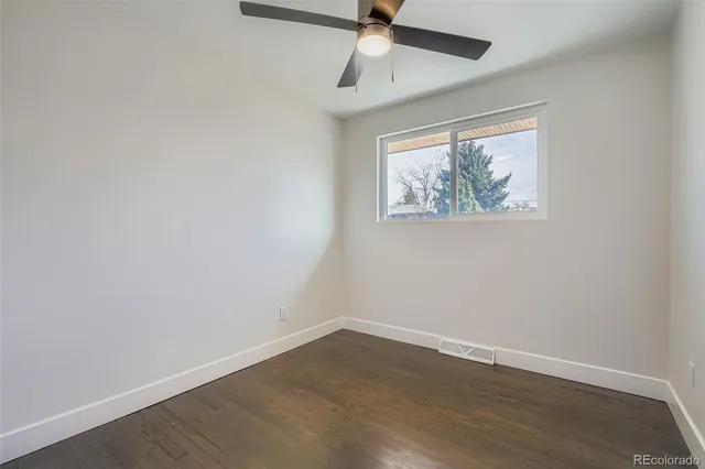 an empty room with wooden floor ceiling fan and window