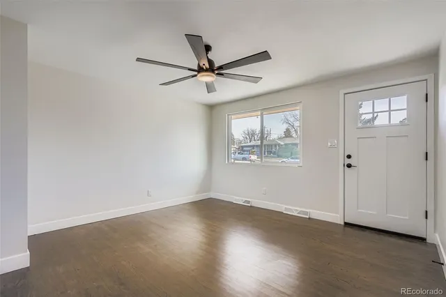an empty room with wooden floor ceiling fan and windows