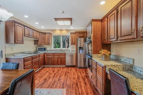 a kitchen with stainless steel appliances granite countertop wooden cabinets a sink dishwasher a stove and a refrigerator with wooden floor