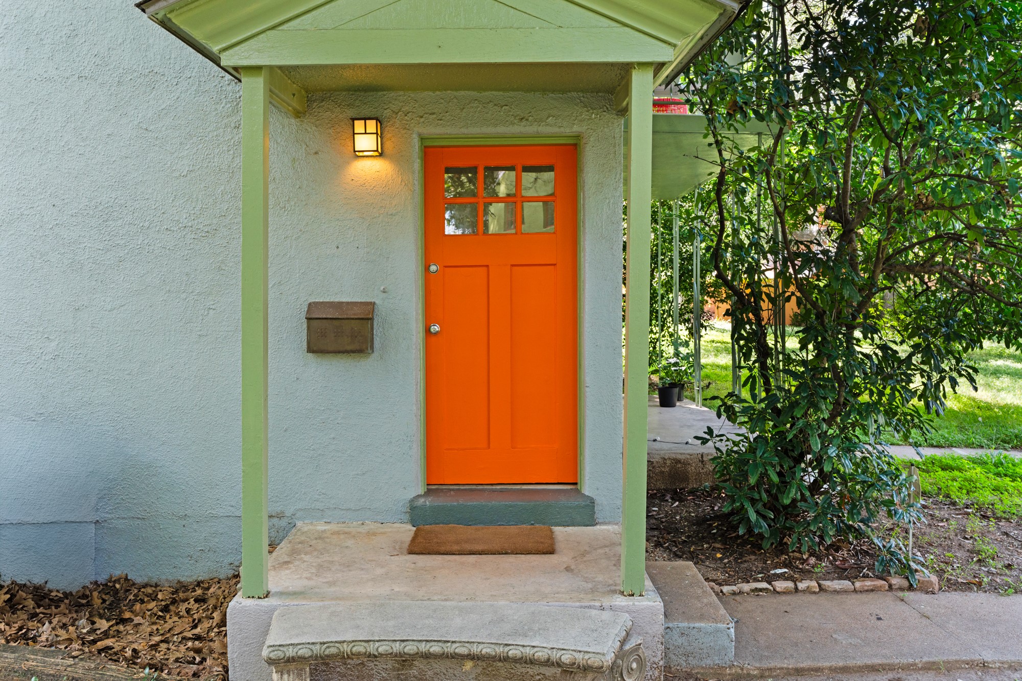 A vibrant orange entry door welcomes guests to this charming, stucco-clad residence.