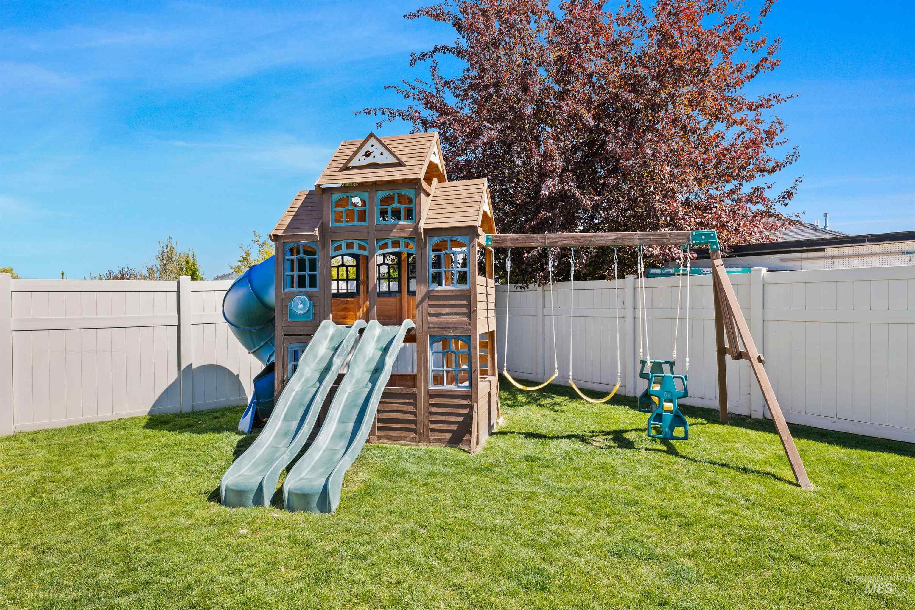 2441 Blick Lane Twin Falls, ID 83301 - Photo 40 of 50 Expansive fenced backyard featuring a play structure with dual slides and a tube slide, an attached swing set with two swings, and a mature tree