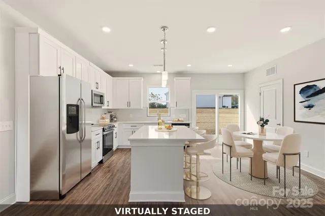 a kitchen with stainless steel appliances kitchen island granite countertop a refrigerator a stove a sink a dining table and chairs with wooden floor