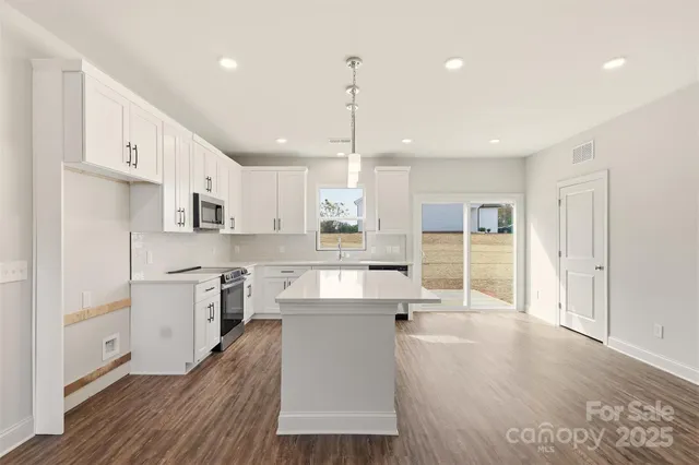a large kitchen with kitchen island a stove a sink a refrigerator and white cabinets with wooden floor