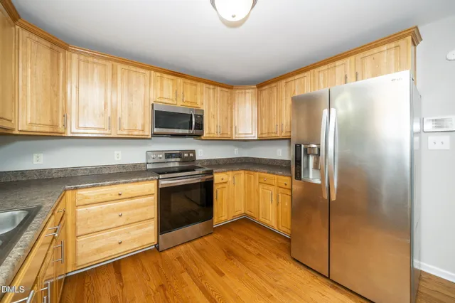 a kitchen with stainless steel appliances granite countertop a refrigerator a stove top oven a sink and dishwasher with wooden floor