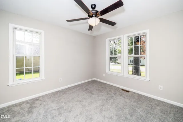 an empty room with ceiling fan and windows