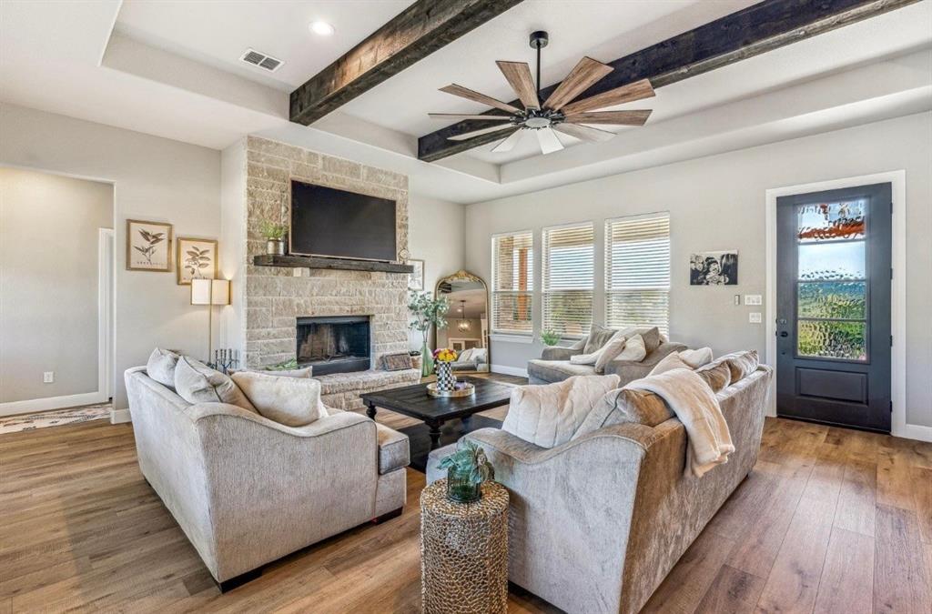 2455 Schooner Way Bluff Dale, TX 76433 - Photo 6 of 37 Living area featuring ceiling fan, wood finished floors, beam ceiling, a stone fireplace, and a raised ceiling