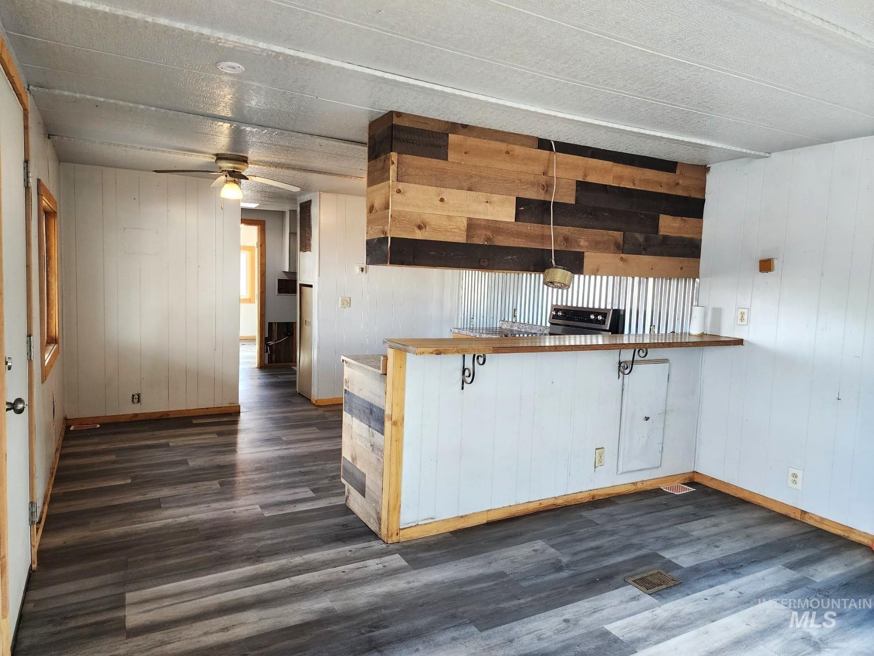1853 McLay Road Vale, OR 97918 - Photo 2 of 8 Kitchen with wooden walls, dark wood-style flooring, a ceiling fan, white cabinets, and decorative light fixtures