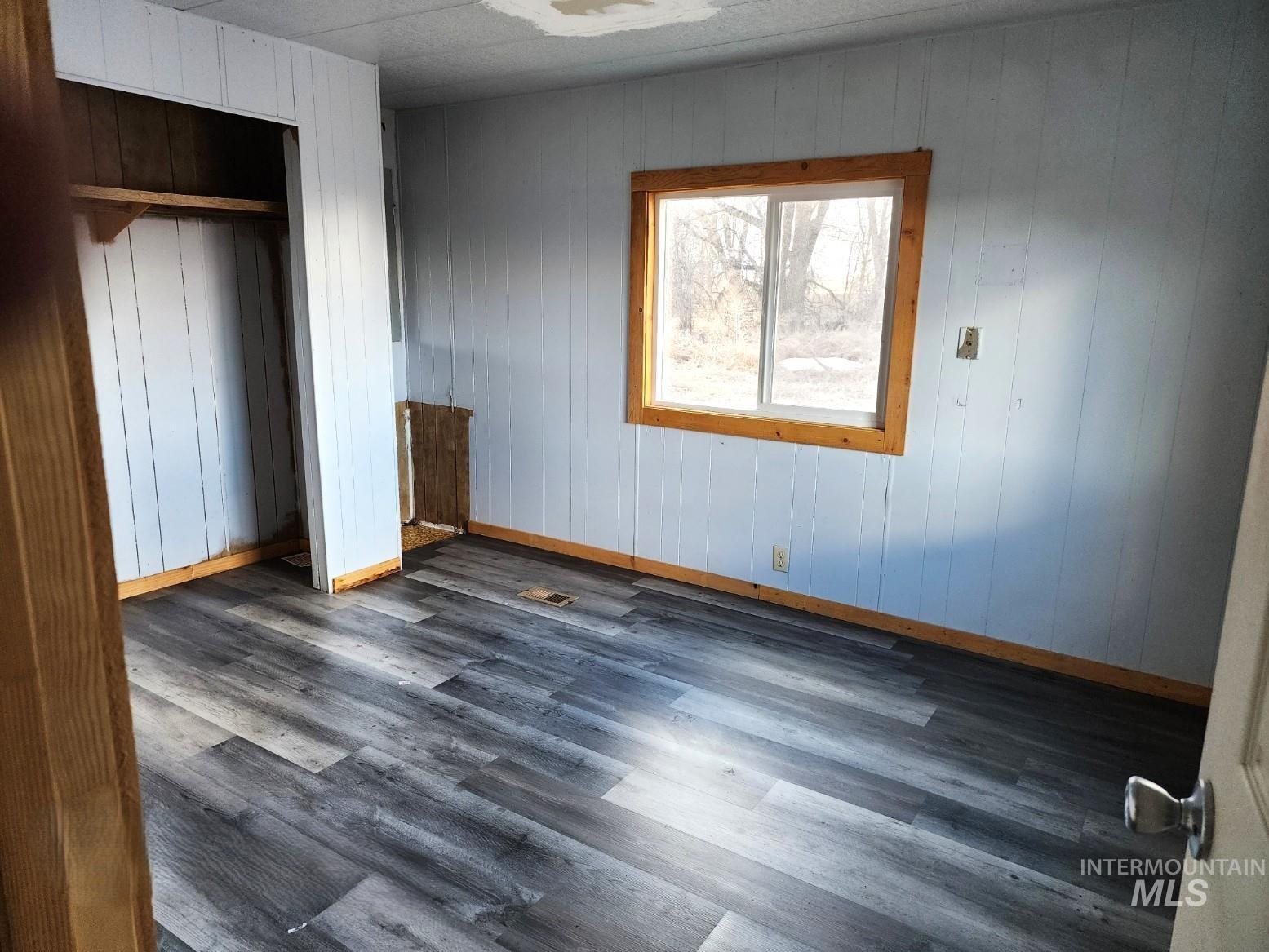 1853 McLay Road Vale, OR 97918 - Photo 5 of 8 Unfurnished bedroom with dark wood-type flooring, wooden walls, and a closet