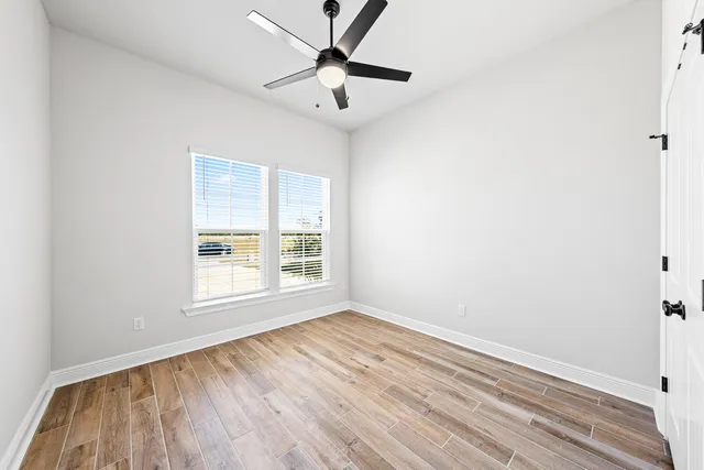 an empty room with wooden floor fan and windows