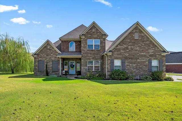 a view of a big yard in front of a brick house with large windows