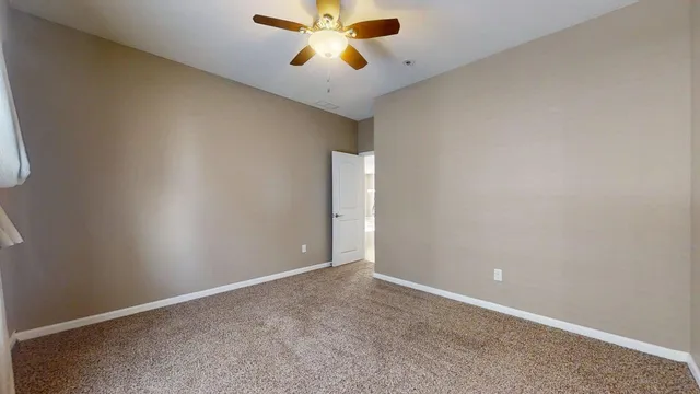 an empty room with chandelier fan and windows