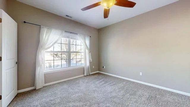 an empty room with chandelier fan and windows