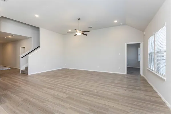 an empty room with wooden floor fan and windows