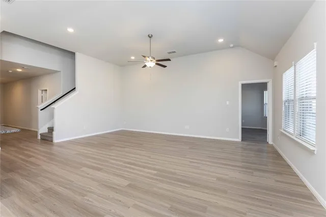 an empty room with wooden floor fan and windows
