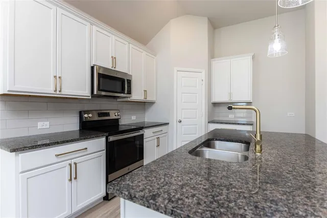 a kitchen with granite countertop a sink dishwasher stove and cabinets