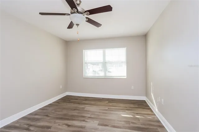 an empty room with wooden floor fan and windows