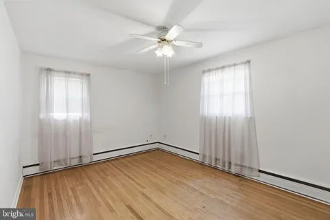 an empty room with wooden floor fan and windows