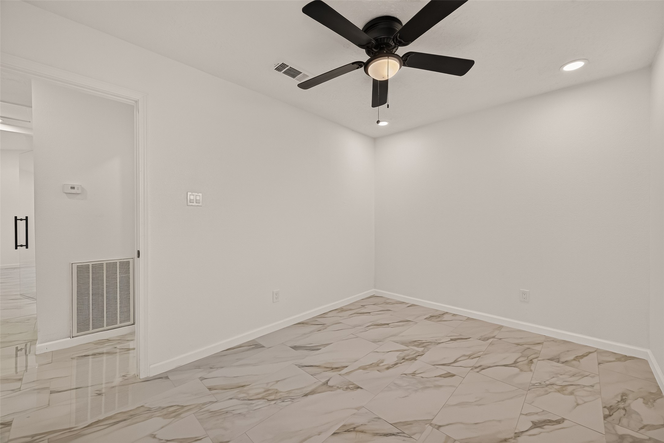 16619 Tibet Road Friendswood, TX 77546 - Photo 18 of 29 This room features a clean, modern design with neutral walls, marble-patterned tile flooring, and a ceiling fan. Recessed lighting adds brightness, and the open doorway leads to the adjacent space, enhancing the room's airy feel.