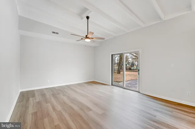 an empty room with wooden floor fan and windows