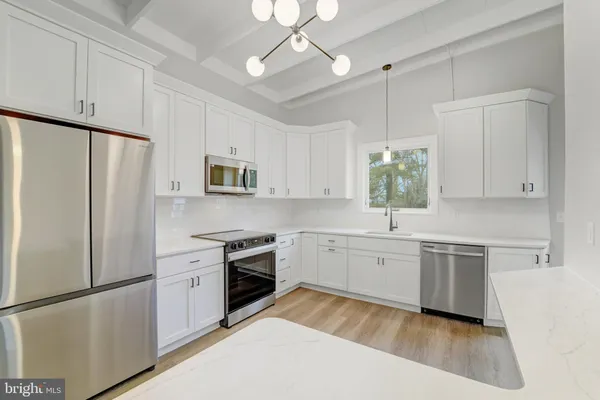 a kitchen with granite countertop a refrigerator a sink dishwasher a oven and white cabinets with wooden floor