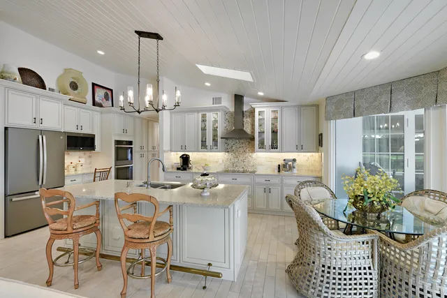 a kitchen with stainless steel appliances kitchen island granite countertop a dining table chairs and a refrigerator