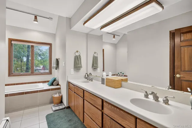 a bathroom with a double vanity sink a large mirror and a bathtub next to a window