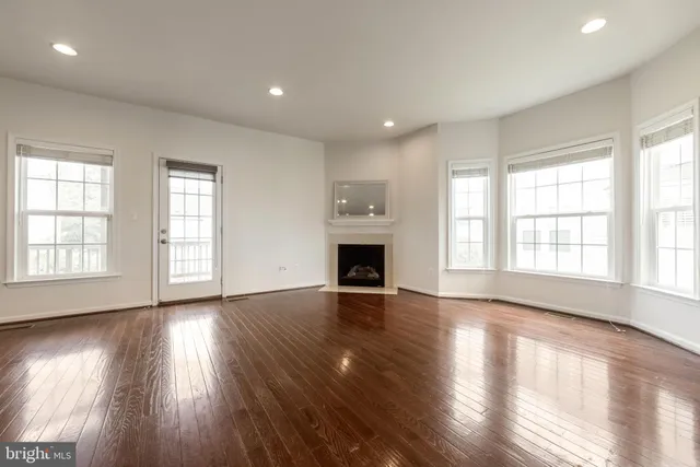 an empty room with wooden floor fireplace and windows