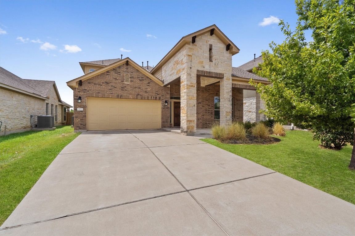 View of front facade featuring a front yard, brick siding, driveway, an attached garage, and stone siding