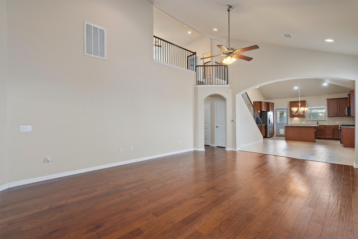 533 Jess Maynard Trail Leander, TX 78641 - Photo 2 of 24 Unfurnished living room featuring dark wood finished floors, a chandelier, arched walkways, a ceiling fan, and high vaulted ceiling