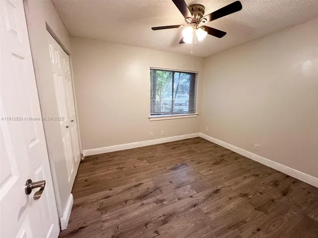 an empty room with wooden floor fan and windows